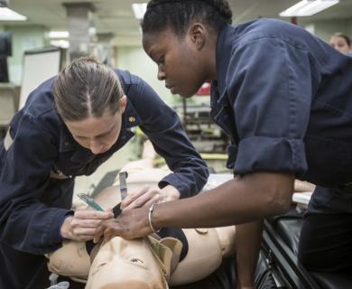 Two female Navy service members prepare simulated person for intubation.