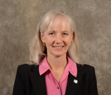 White woman executive with light hair in black suit against brown background