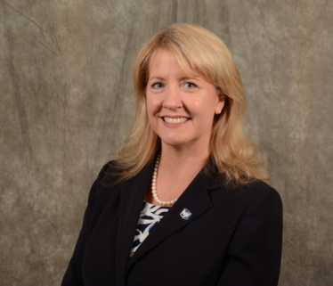 White woman executive with blond hair in dark suit against brown background