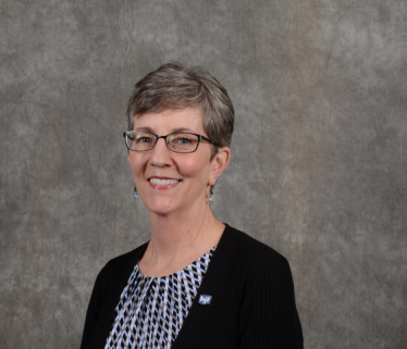 White woman executive with short hair in grey suit against brown background