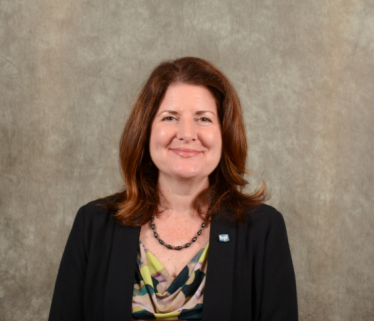 White woman executive with brown hair in black suit against brown background