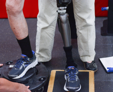 One flesh leg and one prosthesis in blue tennis shoes. Prosthesis leg and foot are on a black balance board.