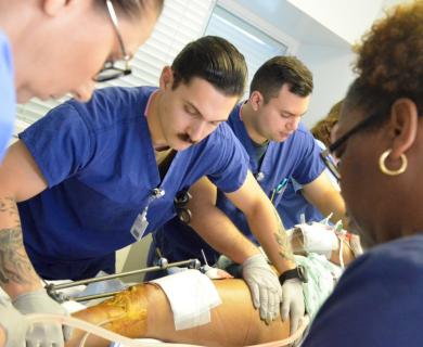 A group of people in medical scrubs work to transport a patient. Patient's leg is seen with wound dressings.