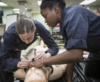 Two female Navy service members prepare simulated person for intubation.