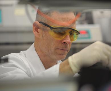 male scientist works with white gloves and protective eyewear.