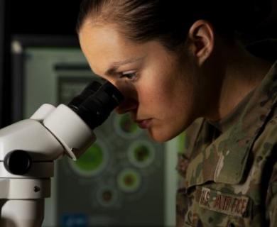 Air Force woman looks into microscope.