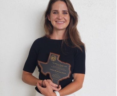 White woman with brown hair wearing a black shirt holding a plaque the shape of the state of Texas
