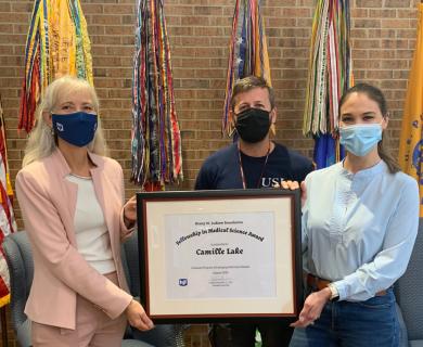 Three people holding a big plaque indicating an award has been given. All are wearing masks.