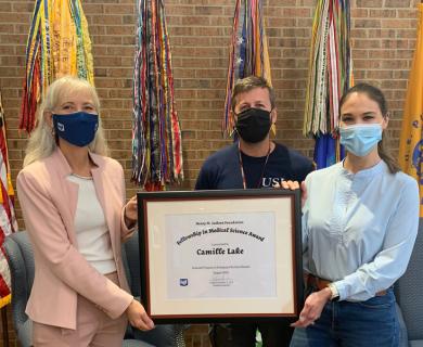 Three people holding a big plaque indicating an award has been given. All are wearing masks.