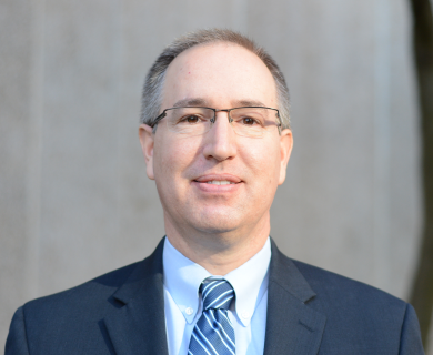 Image of Brian Agan; white man in blue suit against grey background