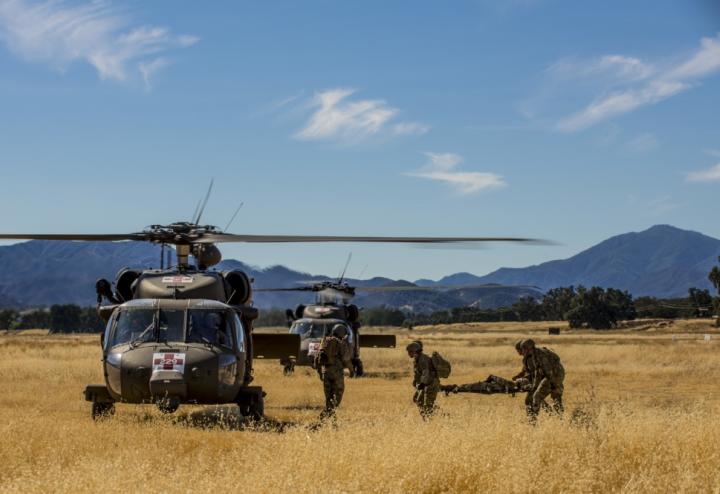 3 army medics transport stretcher into waiting helicopter. Mountains in the background.