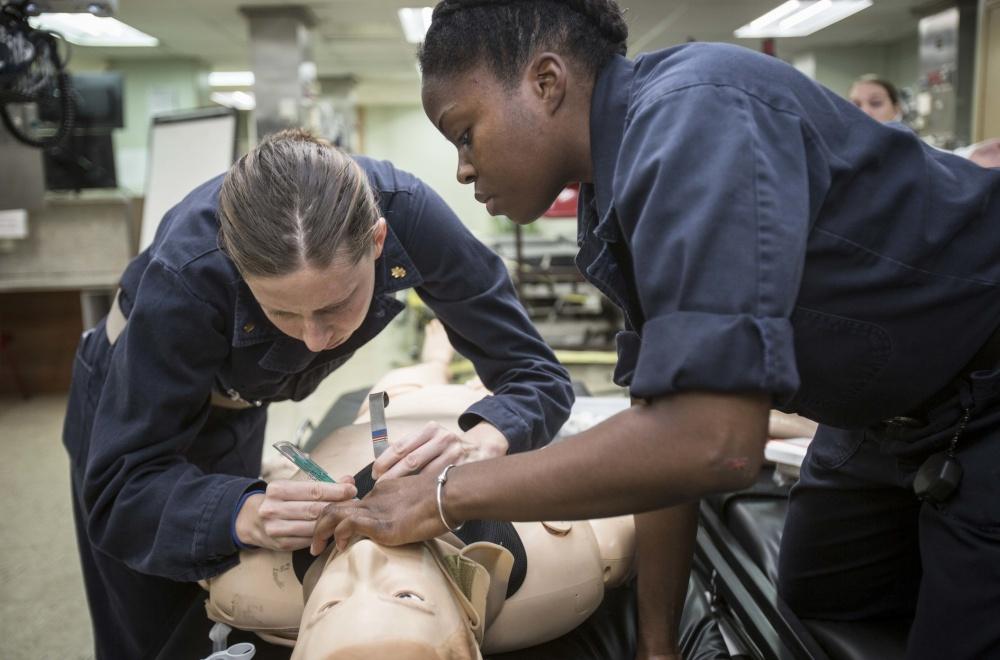 Two female Navy service members prepare simulated person for intubation.
