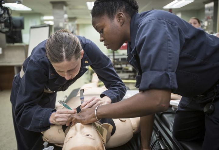 Two female Navy service members prepare simulated person for intubation.