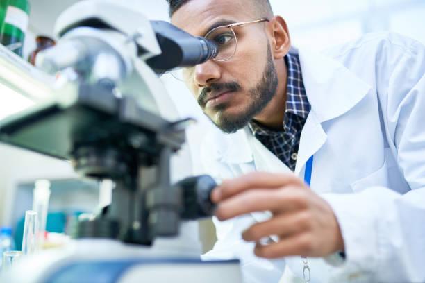 Middle Eastern Man in white lab coat looks into microscope