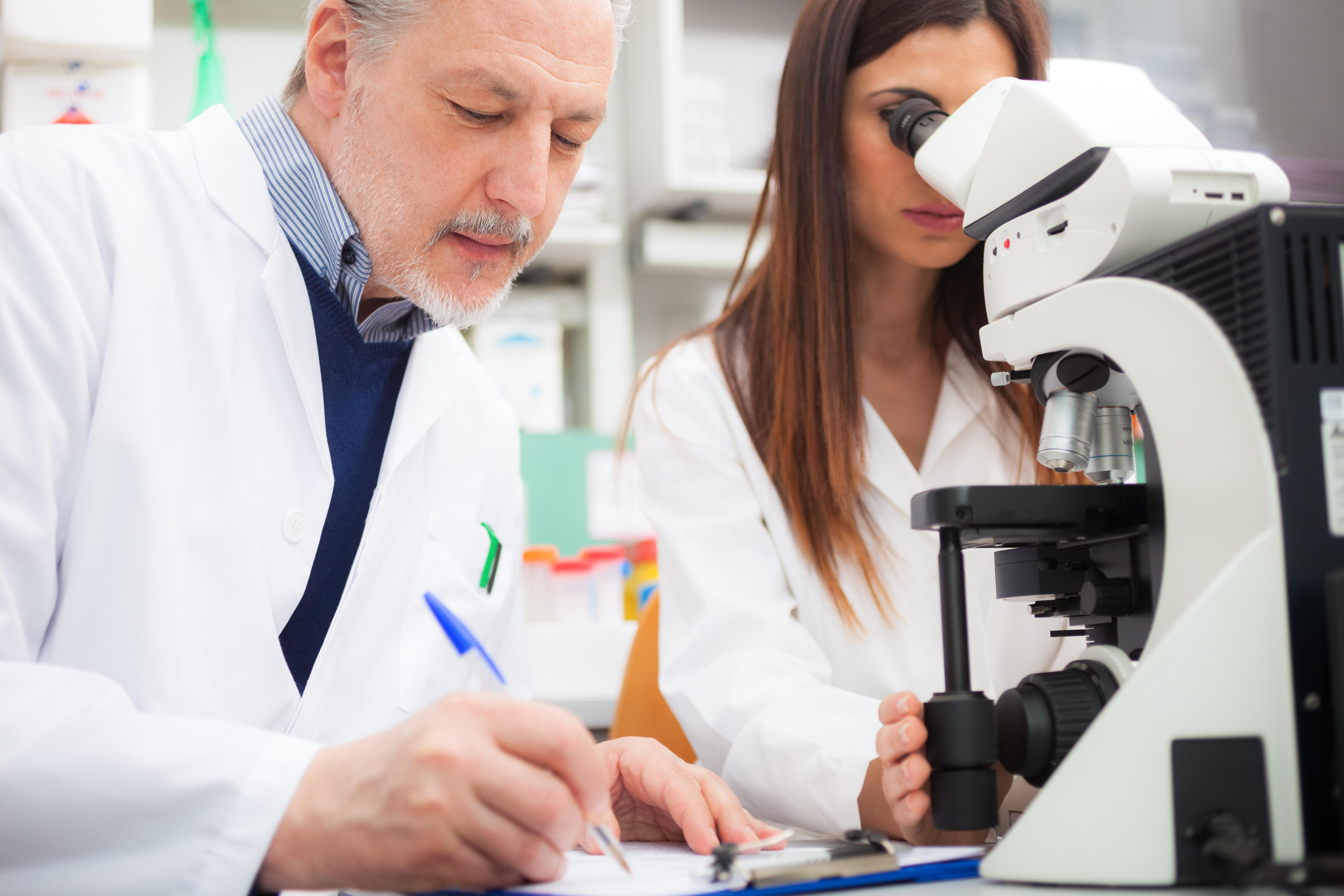 Male and female scientists use microscope while male takes notes