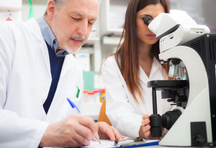 Male and female scientists use microscope while male takes notes Male and female scientists use microscope while male takes notes
