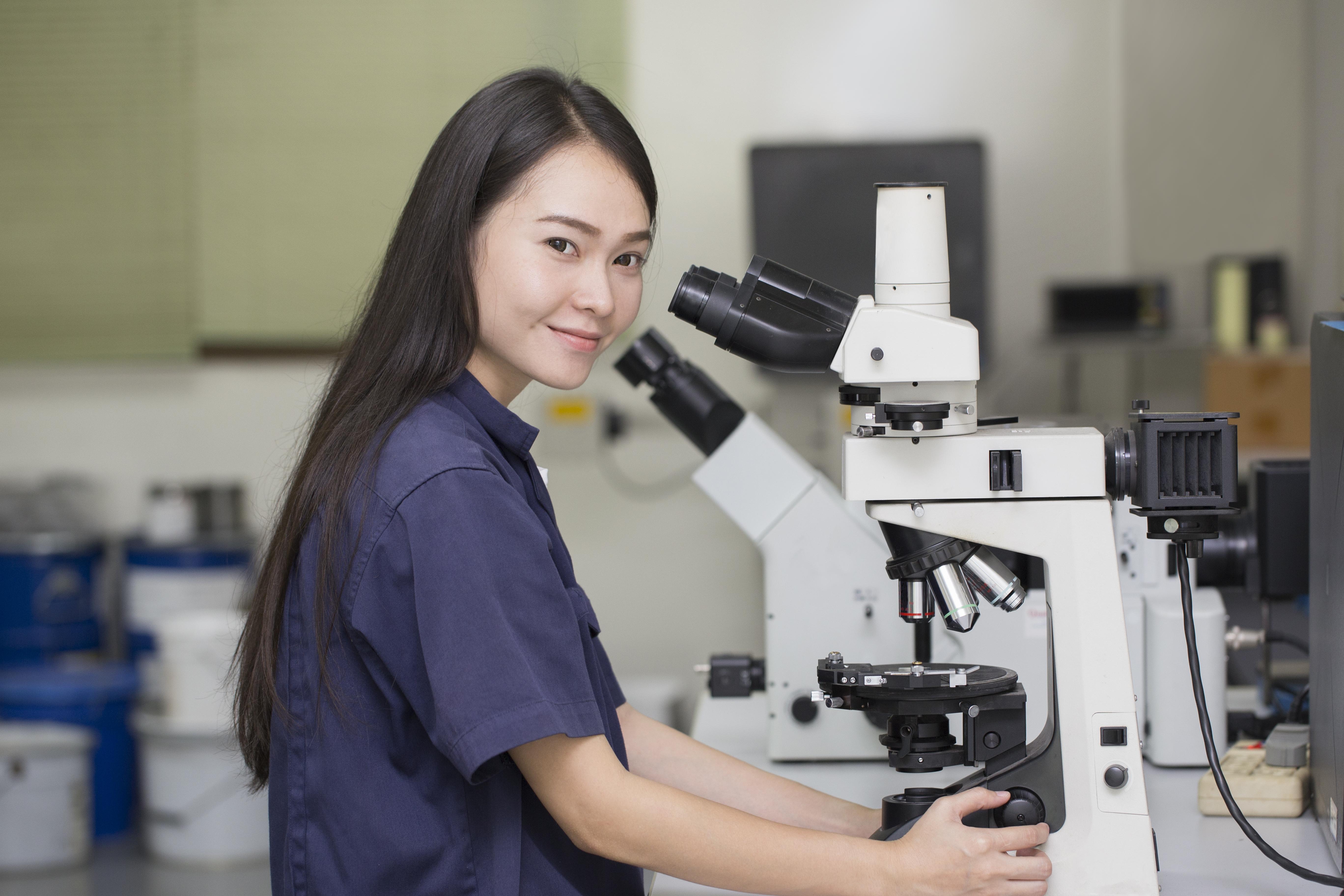 Female scientist looks at camera in front of microscope