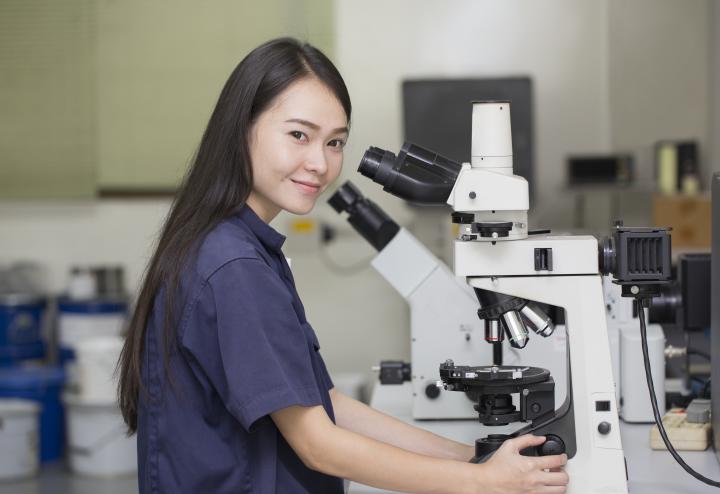 Female scientist looks at camera in front of microscope Female scientist looks at camera in front of microscope