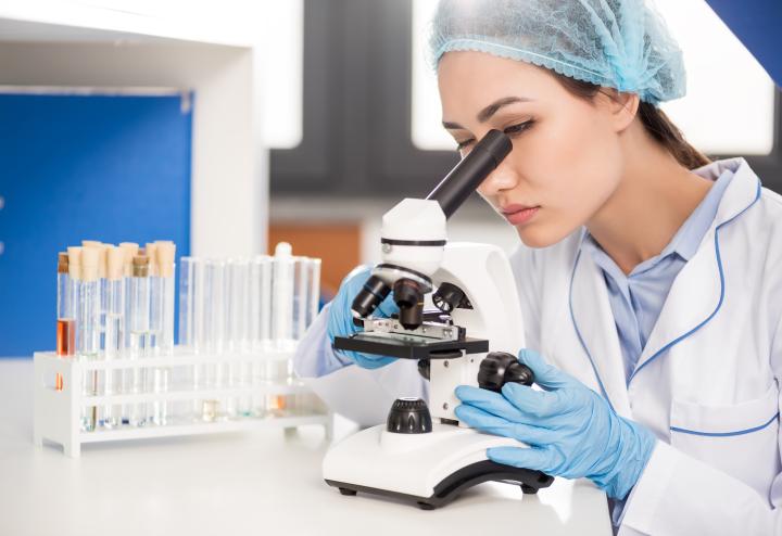 Scientist with microscope and beakers in the background