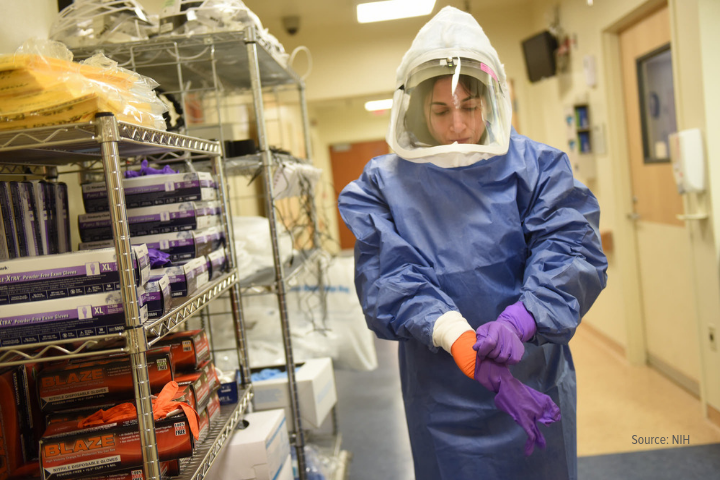 Female scientist fully gowned in containment gear standing next to metal shelves with equipment