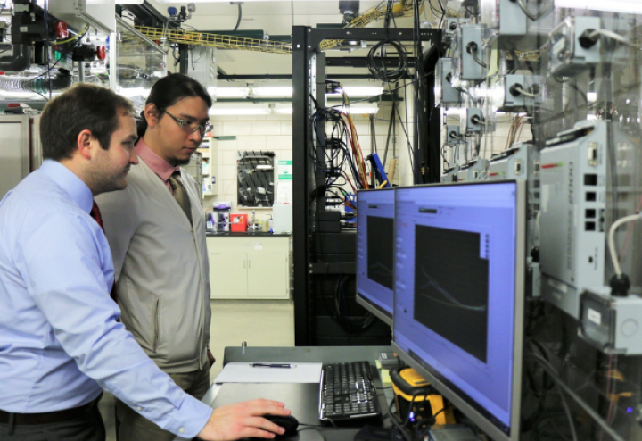 Two men stand and look at computer screens