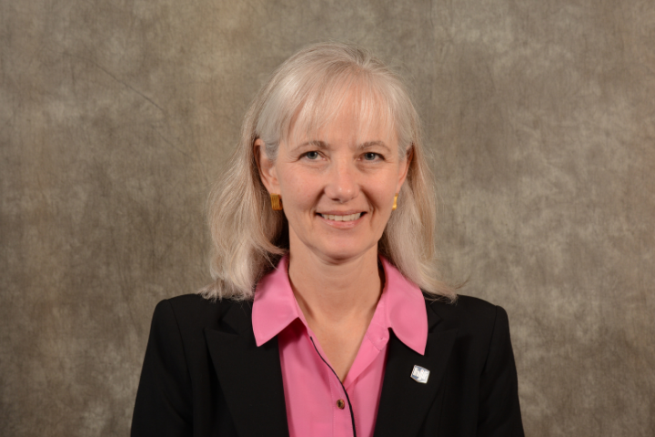 White woman executive with light hair in black suit against brown background