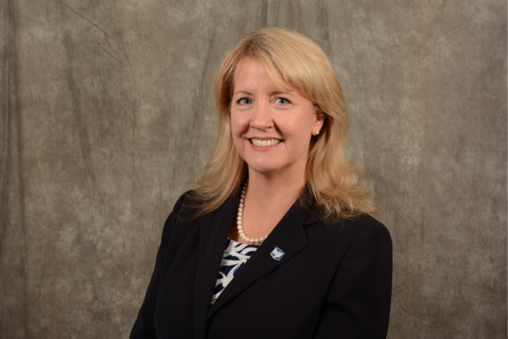 White woman executive with blond hair in dark suit against brown background