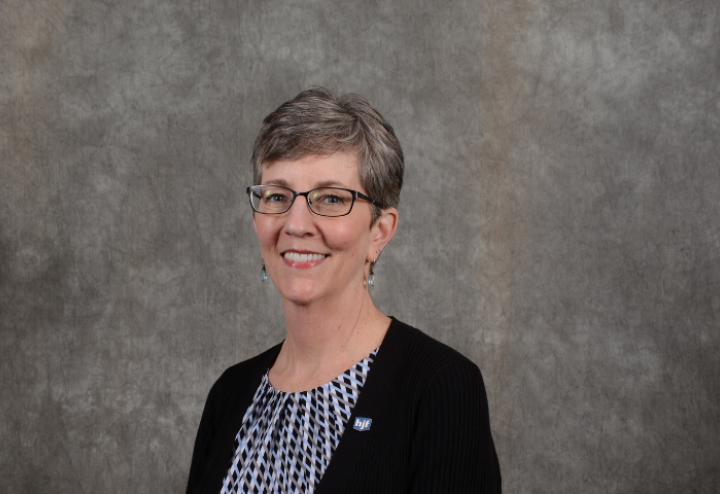 White woman executive with short hair in grey suit against brown background