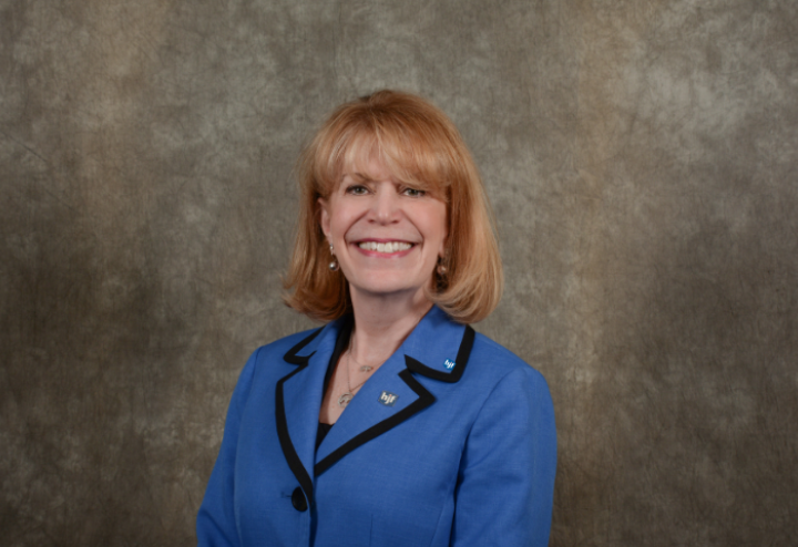 White woman with blond hair in blue suit against brown background