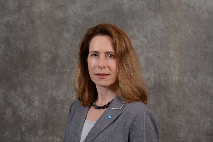 White woman with brown hair in grey suit against brown background