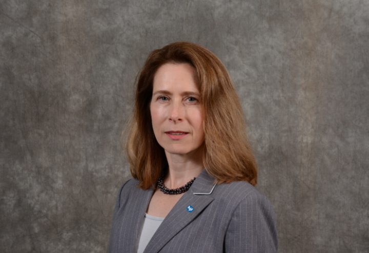 White woman executive with brown hair in grey suit against brown background