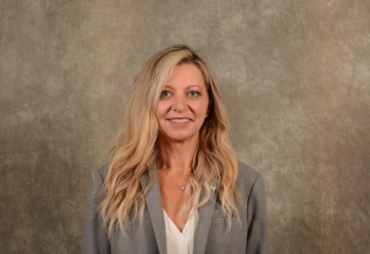 White woman executive with blond hair in grey suit against brown background