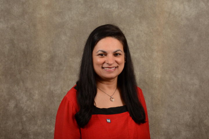 South Asian woman executive in red and black shirt with long black hair against brown background