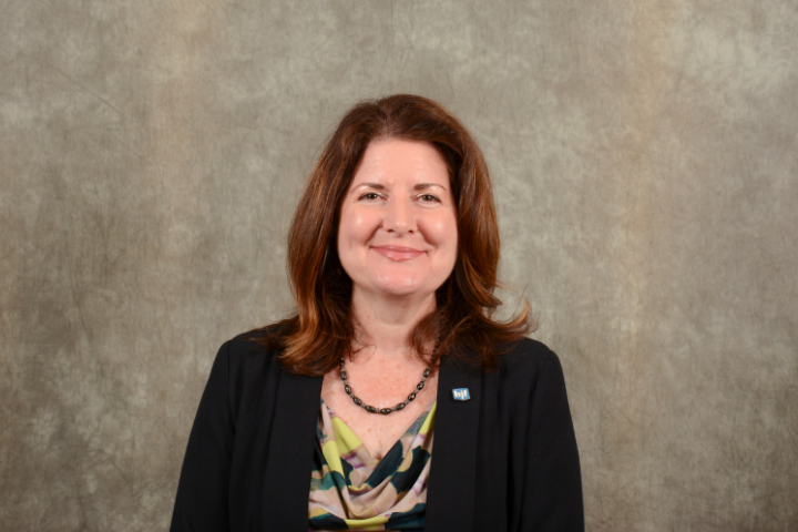 White woman executive with brown hair in black suit against brown background