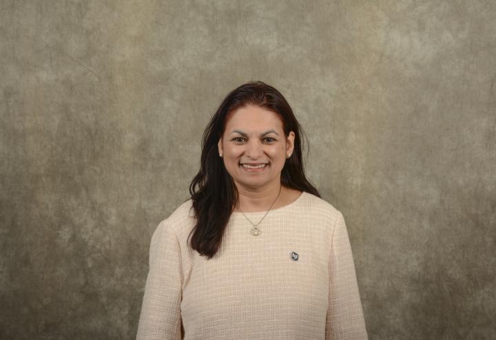 South Asian woman executive in red and black shirt with long black hair against brown background