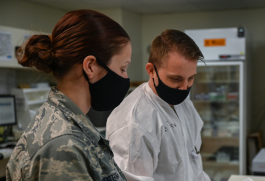 Woman in military uniform stands next to man in lab and shows him paper