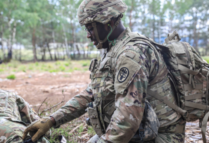 Black man in military gear applies a tourniquet to a leg