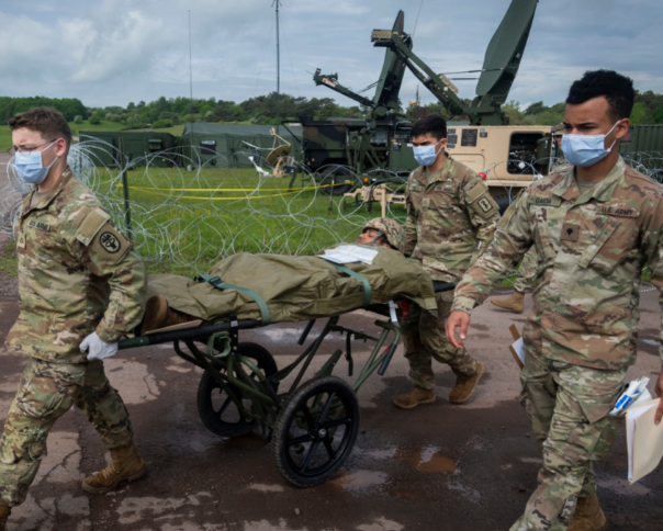 Three military personnel move a man on a stretcher