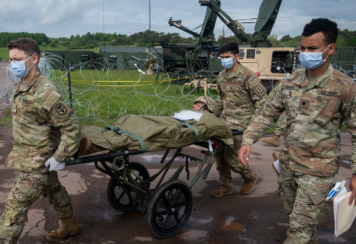 Three military personnel move a man on a stretcher