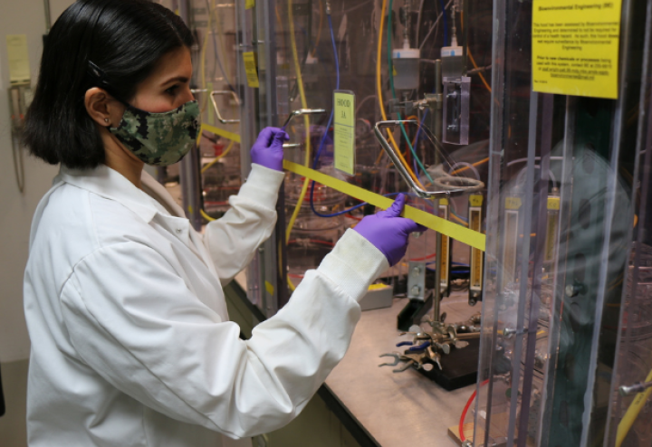 Women in lab coat and mask lifts up glass panel to research machinery