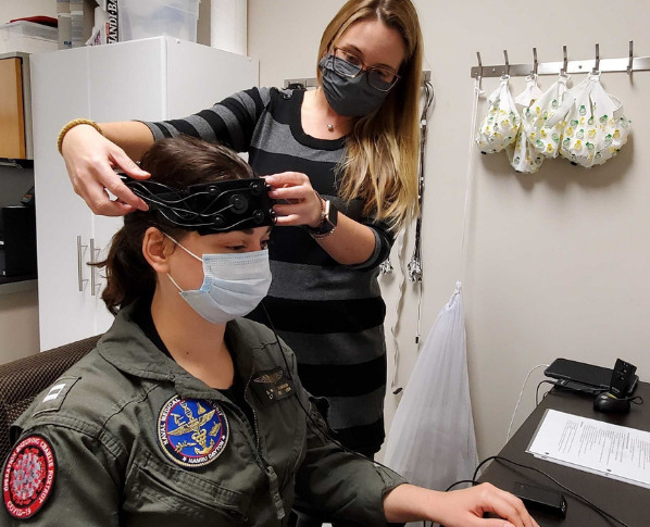 Woman adjusts medical device on the forehead of a woman in Naval Medical Research Unit uniform