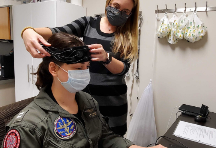 Woman adjusts medical device on the forehead of a woman in Naval Medical Research Unit uniform