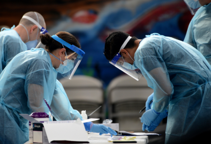 Four people in protective medical gear stand around a table with medical supplies