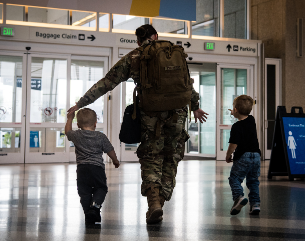 Man in military uniform walks out of airport holding the hands of his two small children