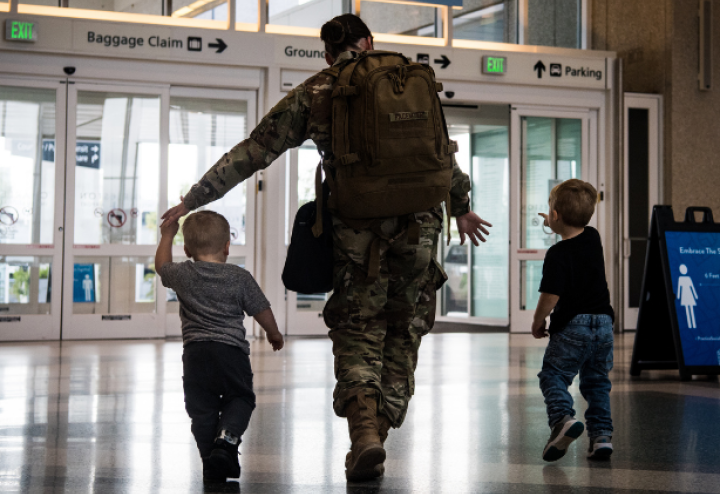 Man in military uniform walks out of airport holding the hands of his two small children