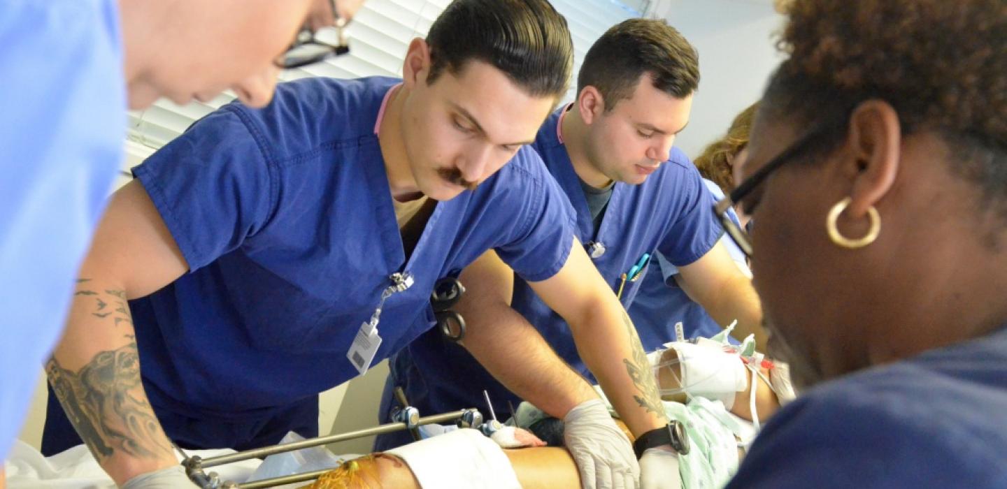 A group of people in medical scrubs work to transport a patient. Patient's leg is seen with wound dressings.