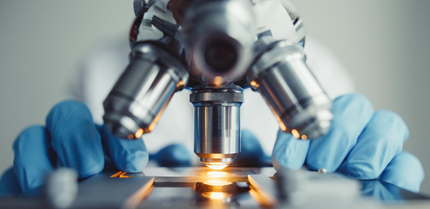 Close up of microscope with blue gloves